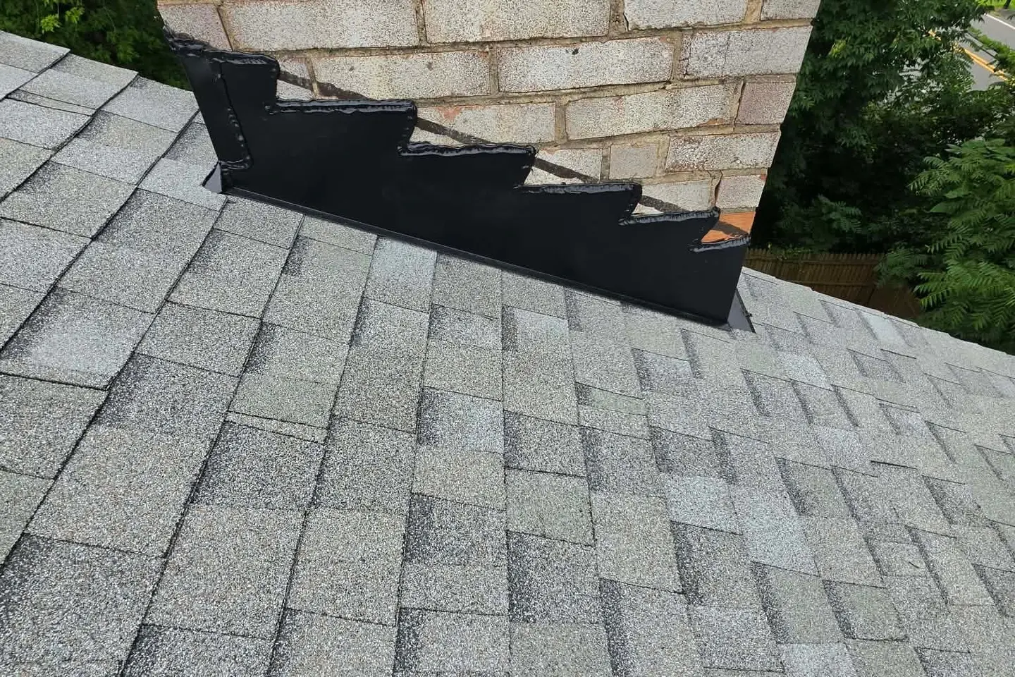 New step flashing and counter flashing where a brick chimney meets light gray shingles