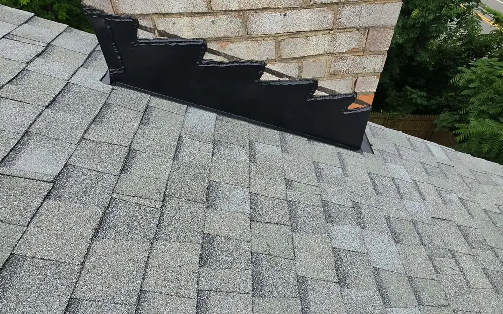 New step flashing and counter flashing where a brick chimney meets light gray shingles