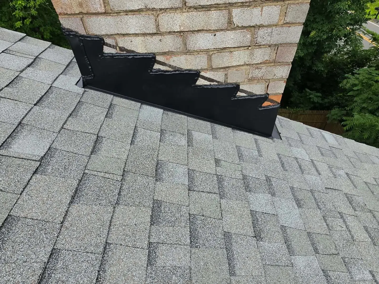 New step flashing and counter flashing where a brick chimney meets light gray shingles