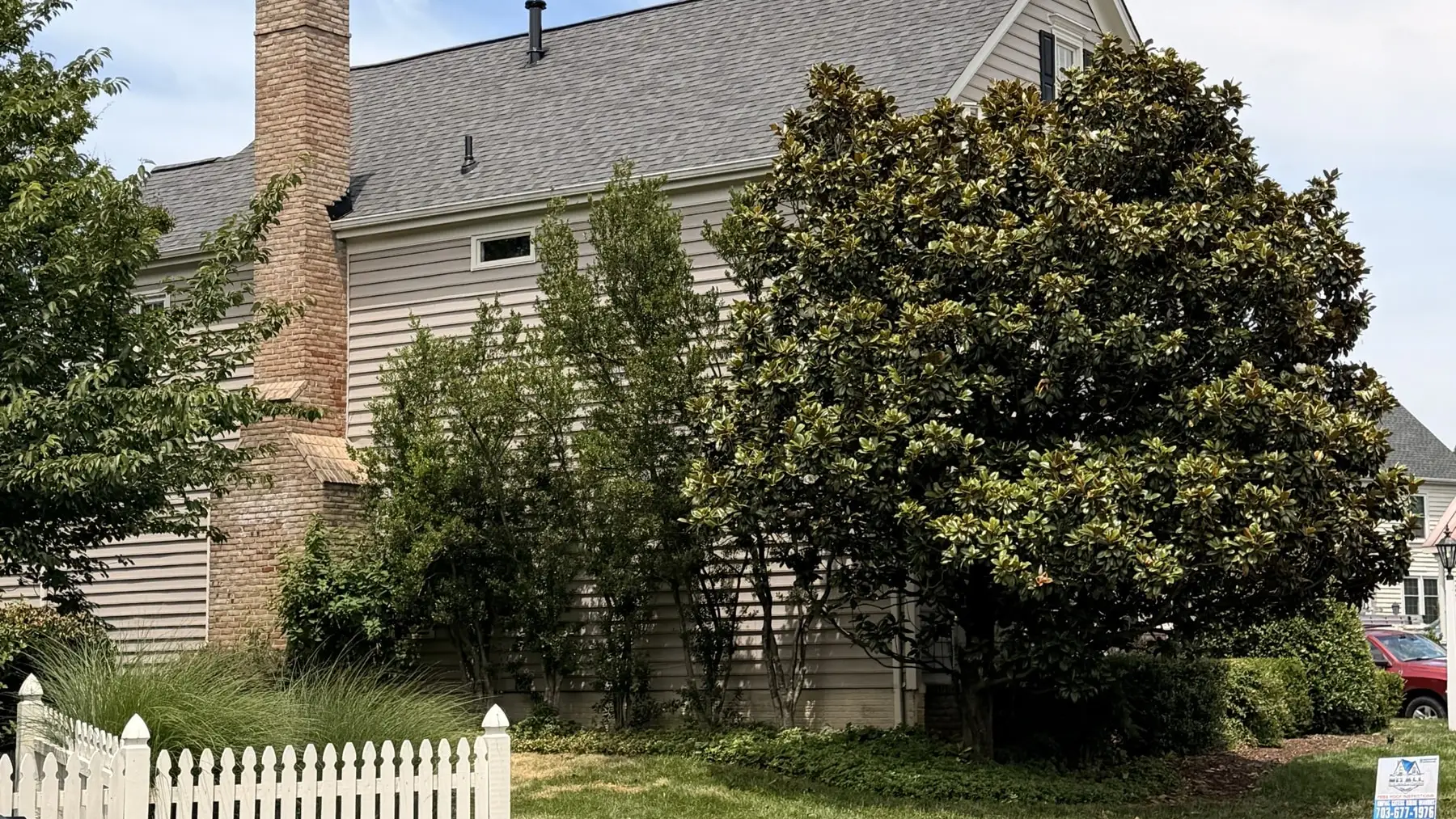 Side of a colonial home with a new gray shingle roof and brick chimney