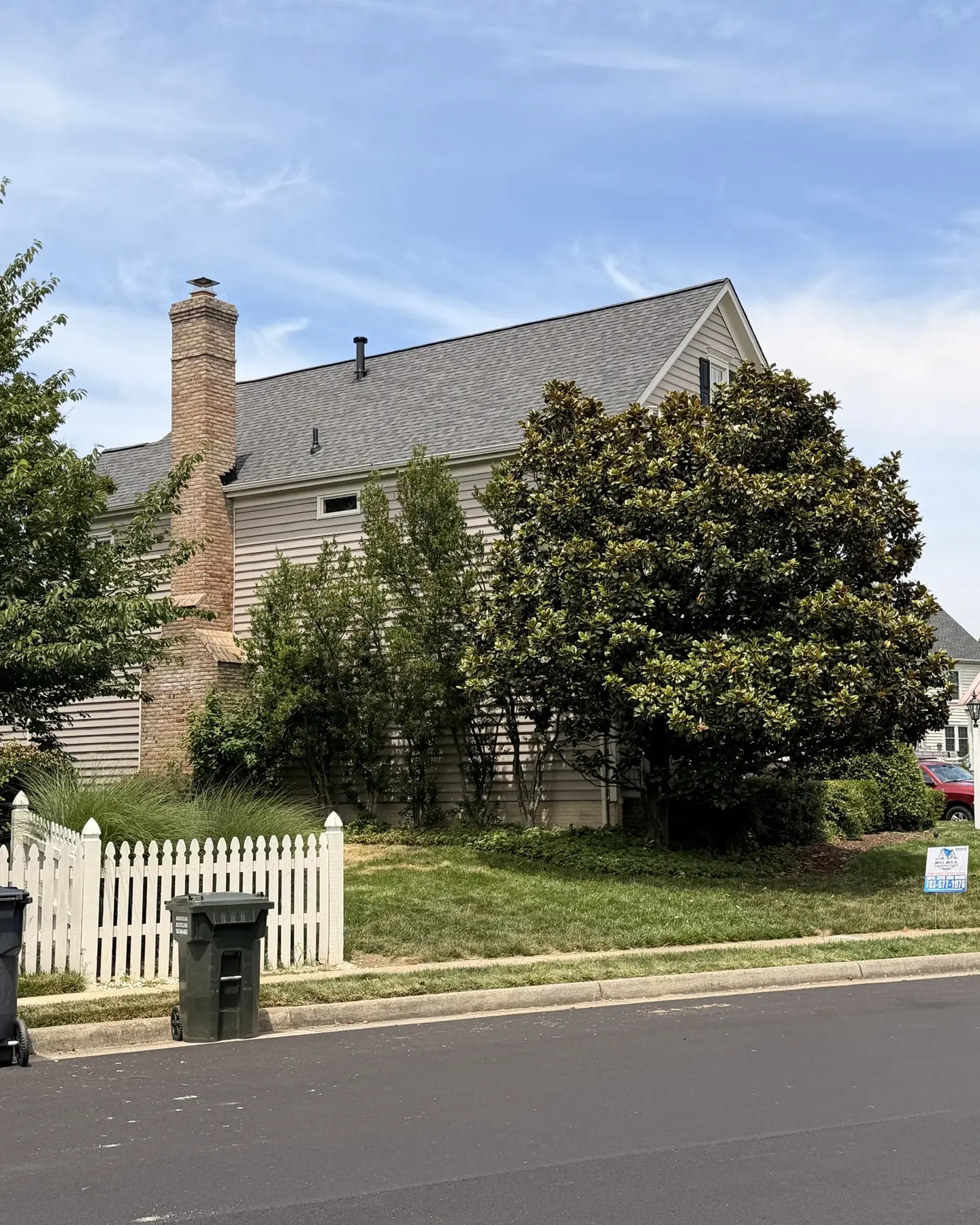 Side of a colonial home with a new gray shingle roof and brick chimney