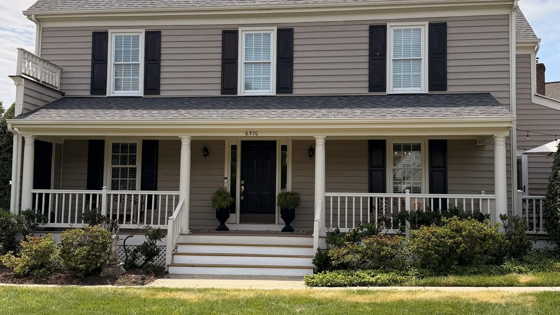 Front of a tan colonial home with a new gray architectural shingle roof and a covered porch