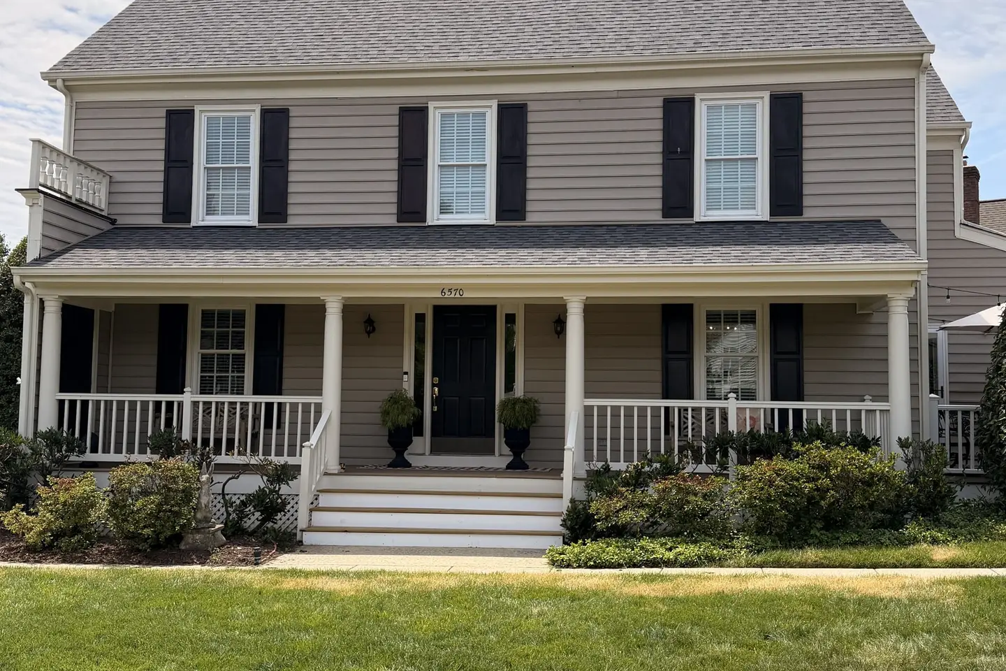 Front of a tan colonial home with a new gray architectural shingle roof and a covered porch