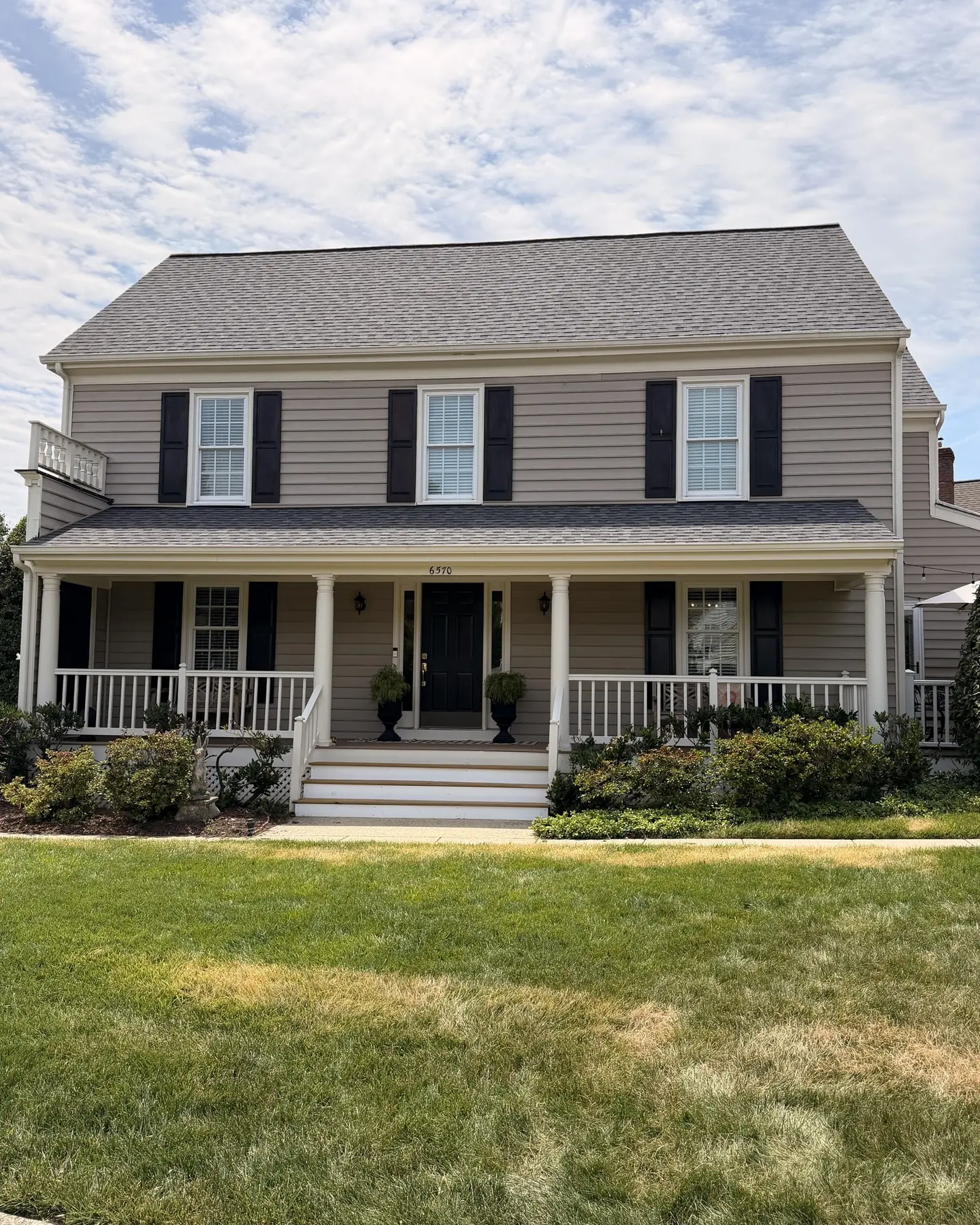 Front of a tan colonial home with a new gray architectural shingle roof and a covered porch