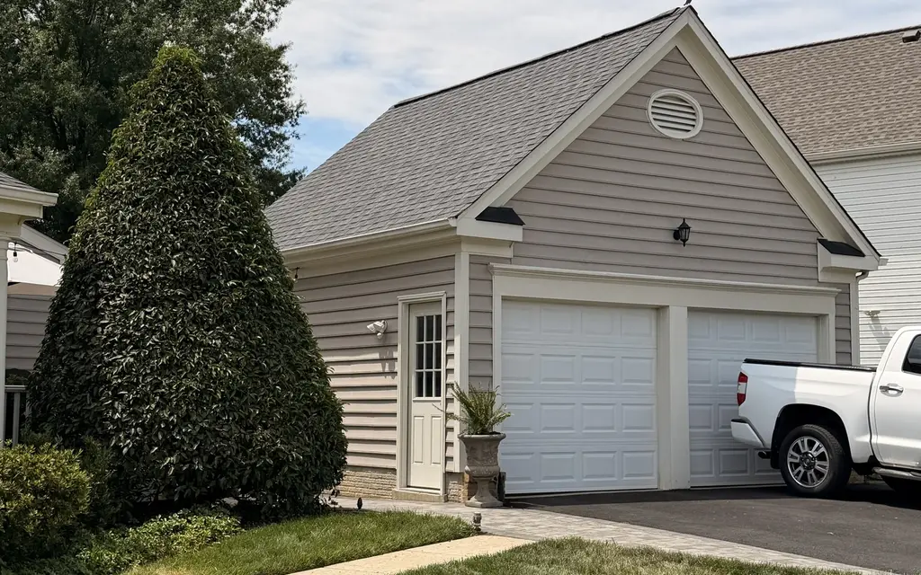 Detached garage with a new gray shingle roof beside a white pickup truck