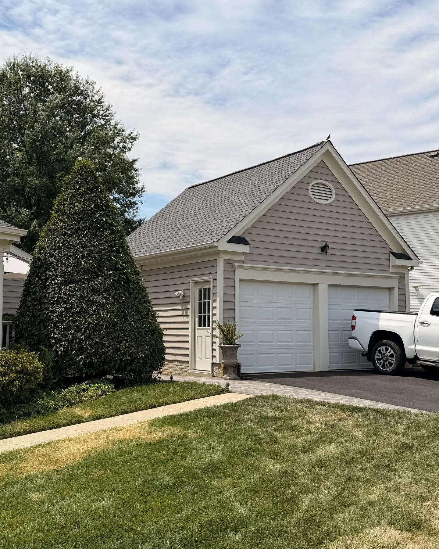 Detached garage with a new gray shingle roof beside a white pickup truck
