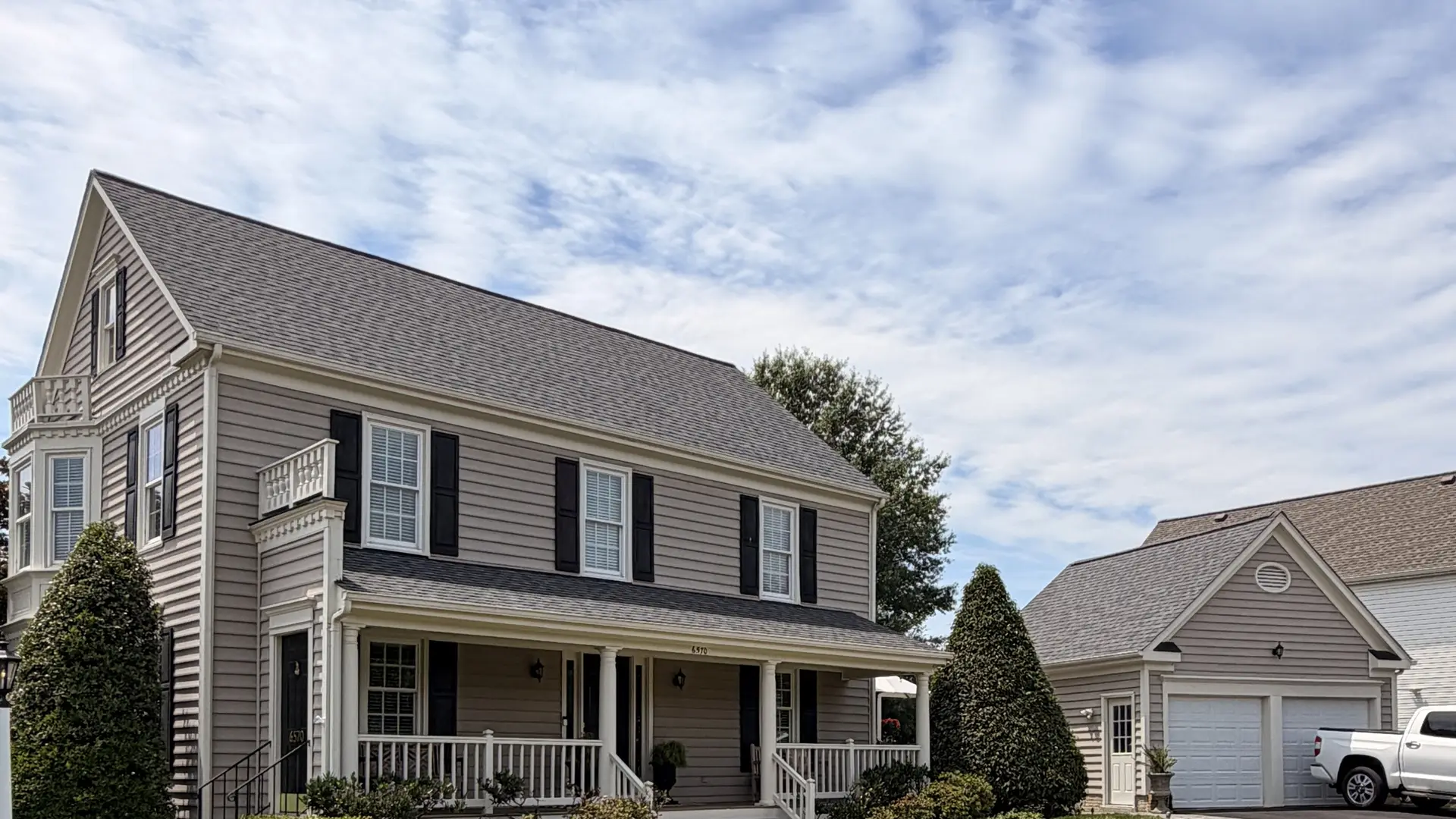 New gray architectural shingle roof on a tan colonial home, seen from the street, a roof replacement by RC All Exteriors