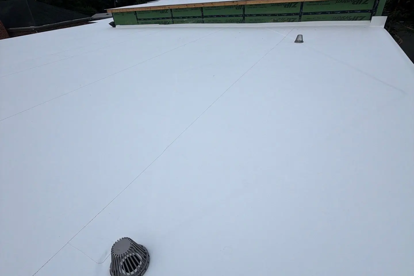 New white TPO membrane on a flat roof with a drain, installed by RC All Exteriors
