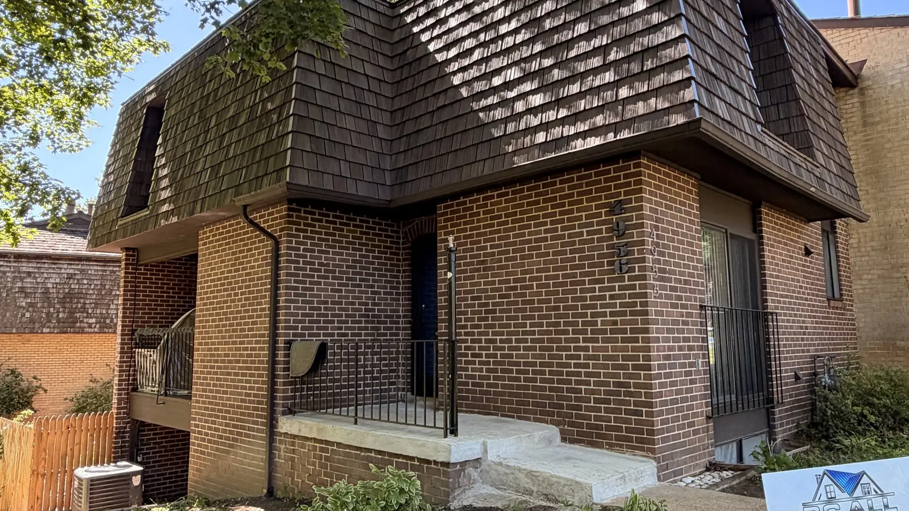 Brick townhouse with a new dark brown mansard roof and the RC All Exteriors yard sign