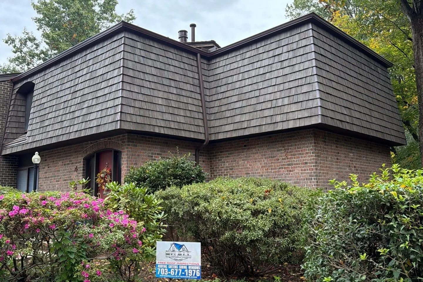 Brick home with a new Brava synthetic shake mansard roof and the RC All Exteriors yard sign by the azaleas