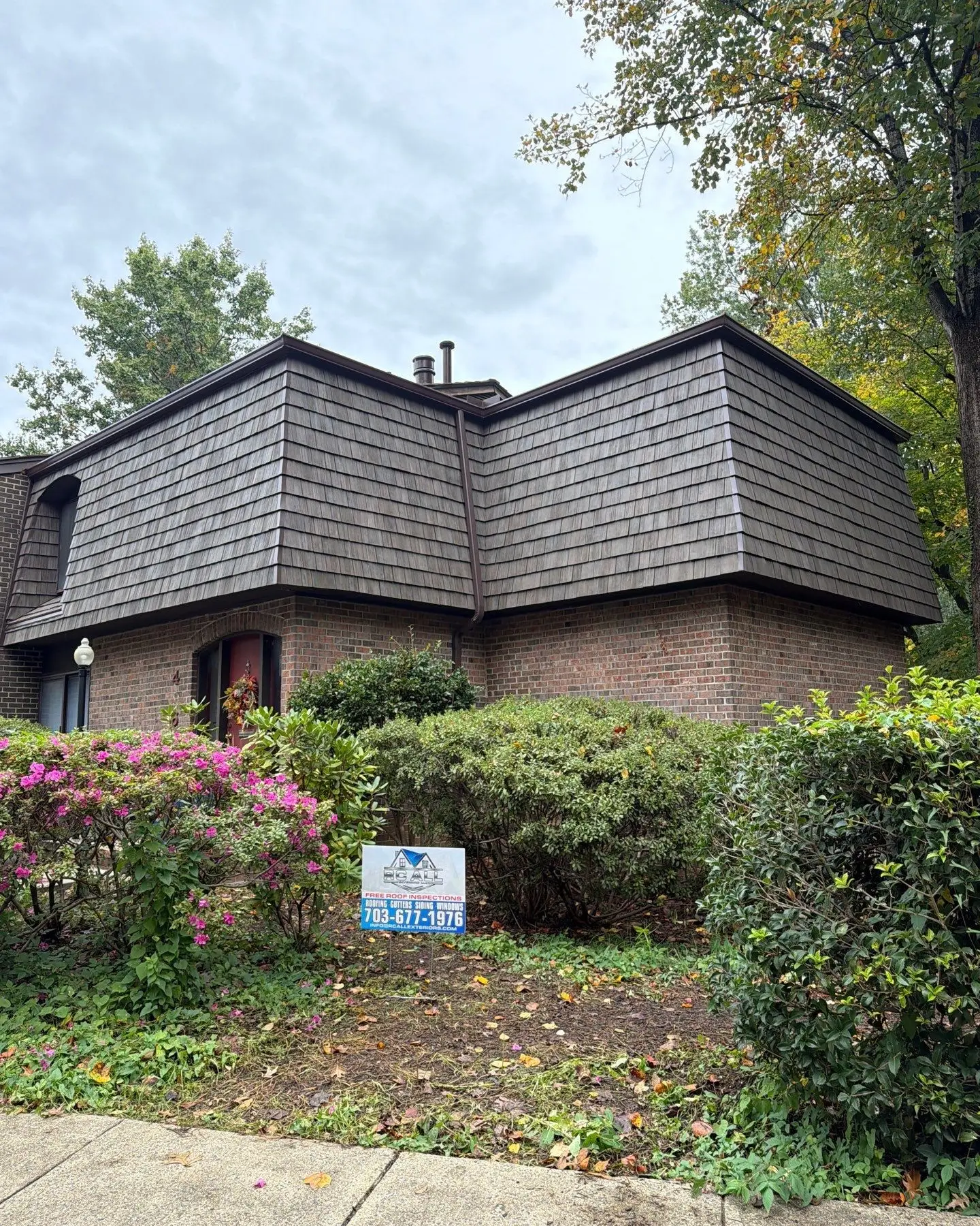Brick home with a new Brava synthetic shake mansard roof and the RC All Exteriors yard sign by the azaleas