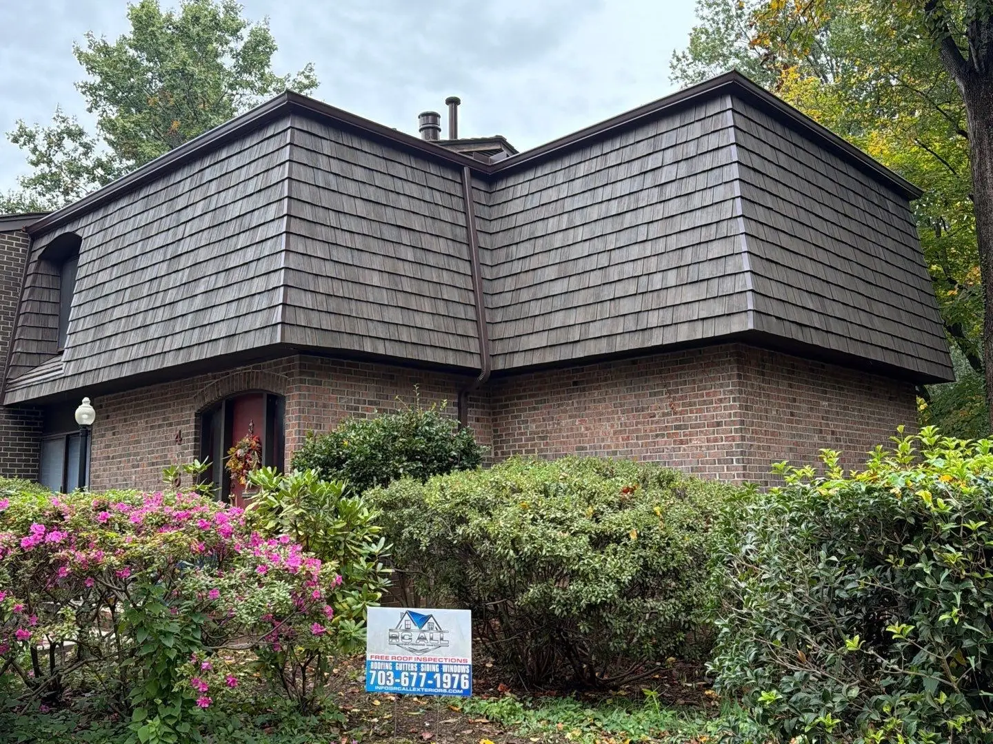Brick home with a new Brava synthetic shake mansard roof and the RC All Exteriors yard sign by the azaleas