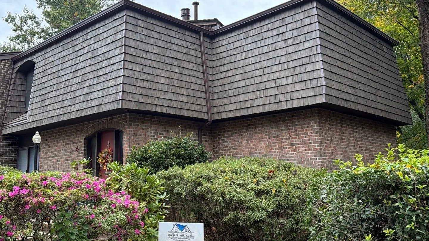 Brick home with a new Brava synthetic shake mansard roof and the RC All Exteriors yard sign by the azaleas